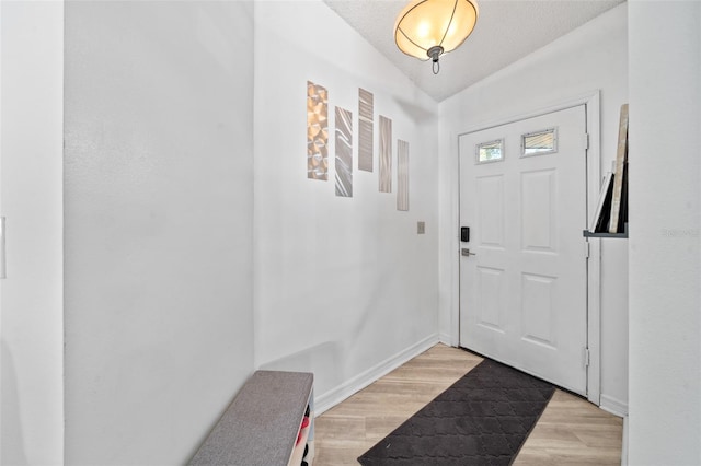 entrance foyer featuring vaulted ceiling, a textured ceiling, and light hardwood / wood-style flooring