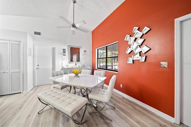 dining space featuring a textured ceiling, high vaulted ceiling, light wood-type flooring, and ceiling fan