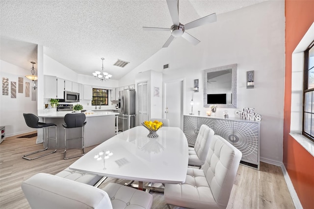 dining space featuring high vaulted ceiling, ceiling fan with notable chandelier, a textured ceiling, and light wood-type flooring