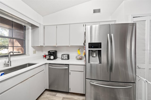 kitchen with appliances with stainless steel finishes, sink, a textured ceiling, lofted ceiling, and white cabinets