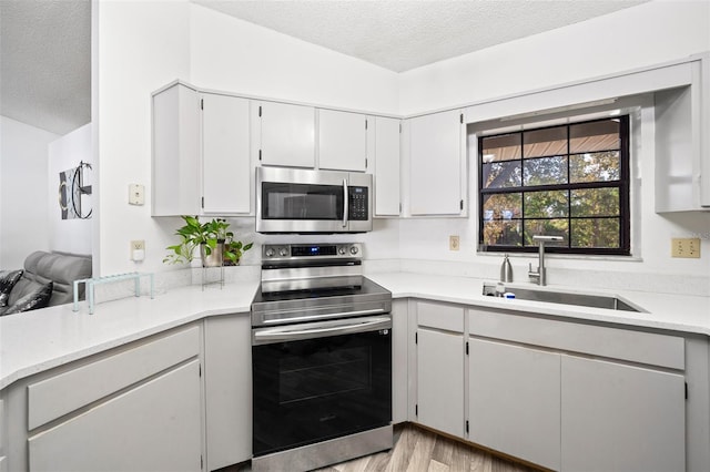 kitchen with sink, appliances with stainless steel finishes, light hardwood / wood-style flooring, and a textured ceiling