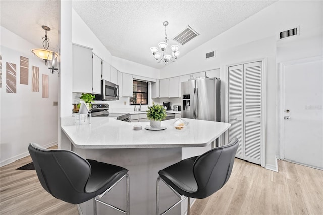 kitchen with lofted ceiling, hanging light fixtures, stainless steel appliances, white cabinetry, and a textured ceiling