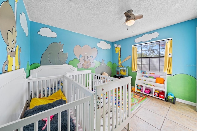 bedroom with a nursery area, a textured ceiling, and ceiling fan