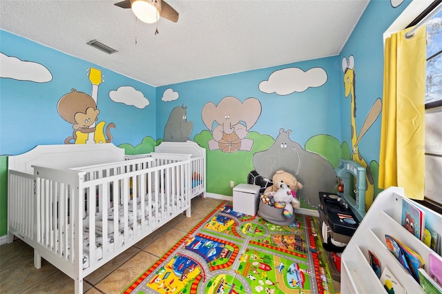 tiled bedroom with a textured ceiling, a crib, and ceiling fan