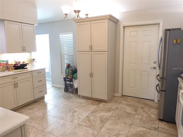 kitchen featuring stainless steel fridge, light stone countertops, a chandelier, cream cabinetry, and decorative light fixtures