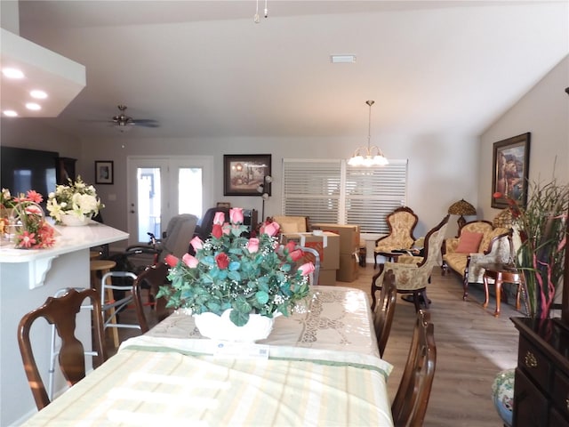 dining space featuring hardwood / wood-style floors, ceiling fan with notable chandelier, and vaulted ceiling