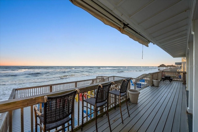 deck at dusk featuring a water view and a beach view