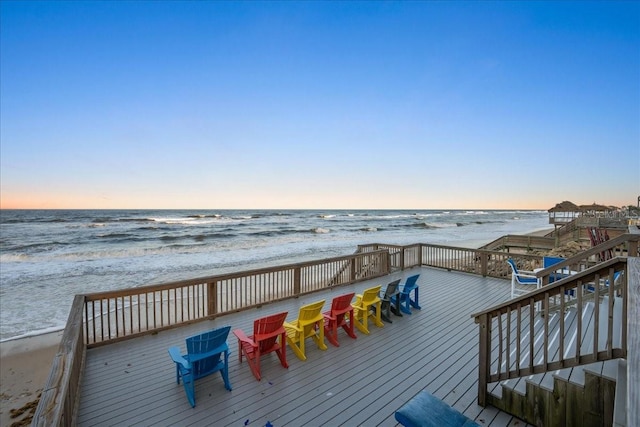 deck at dusk featuring a view of the beach and a water view