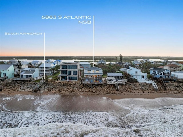 aerial view at dusk featuring a water view and a beach view