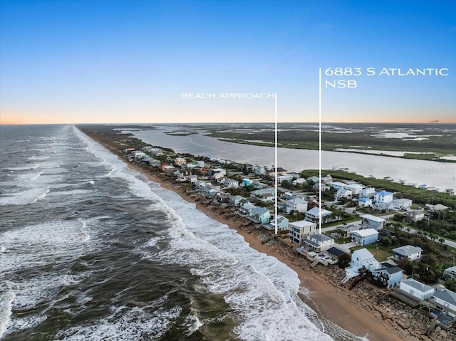 aerial view at dusk with a water view and a beach view