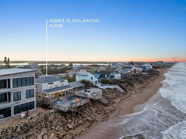 aerial view at dusk featuring a water view and a beach view