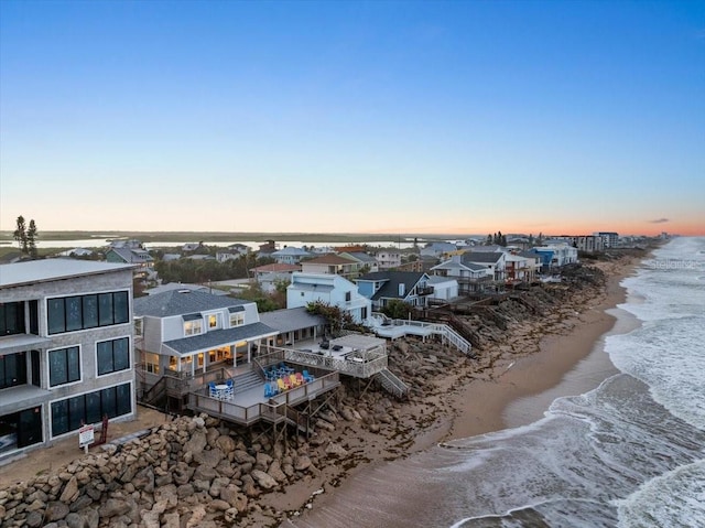 aerial view at dusk featuring a water view and a view of the beach