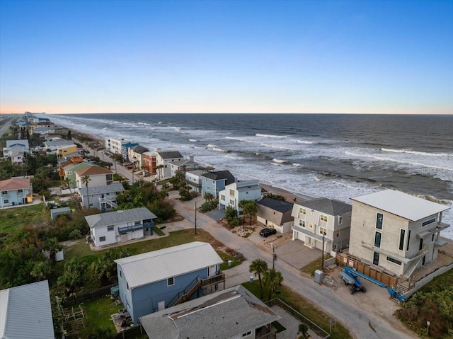 aerial view at dusk featuring a water view and a view of the beach