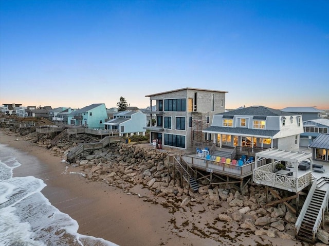 back house at dusk with a deck with water view and a beach view