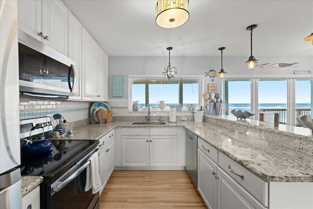 kitchen with appliances with stainless steel finishes, decorative light fixtures, white cabinetry, and light hardwood / wood-style floors