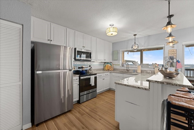 kitchen featuring a kitchen breakfast bar, hanging light fixtures, white cabinets, appliances with stainless steel finishes, and light hardwood / wood-style floors