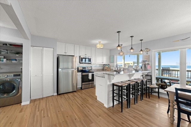 kitchen featuring washer / dryer, appliances with stainless steel finishes, kitchen peninsula, white cabinets, and light hardwood / wood-style flooring