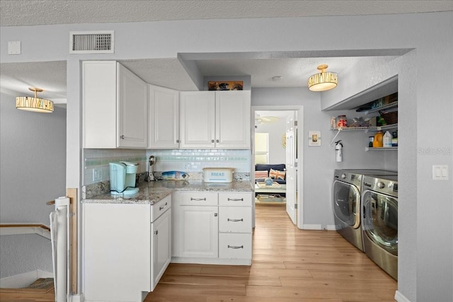 kitchen featuring light stone countertops, washing machine and dryer, light wood-type flooring, backsplash, and white cabinets