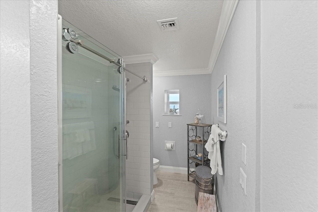 bathroom with a textured ceiling, wood-type flooring, toilet, ornamental molding, and a shower with shower door