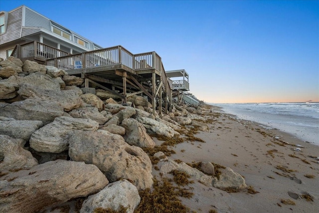 property exterior at dusk featuring a deck with water view and a view of the beach