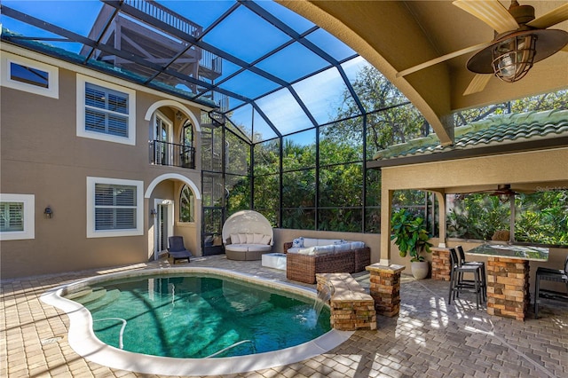 view of pool featuring glass enclosure, ceiling fan, exterior bar, and a patio