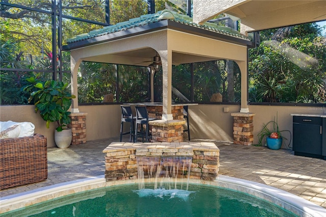 view of pool featuring exterior bar, pool water feature, ceiling fan, a lanai, and a patio area