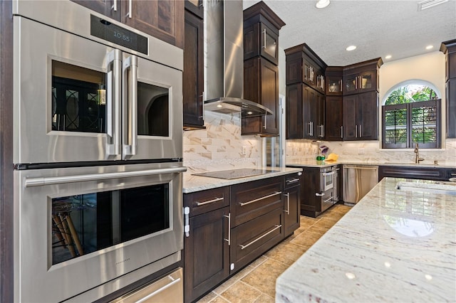 kitchen with tasteful backsplash, light stone counters, wall chimney exhaust hood, and appliances with stainless steel finishes