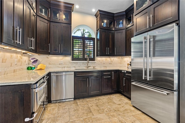 kitchen with light stone counters, sink, dark brown cabinetry, and stainless steel appliances