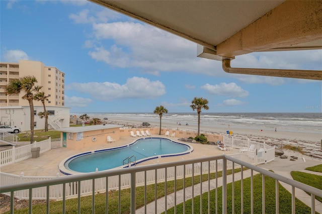 view of swimming pool featuring a patio area, a water view, and a view of the beach