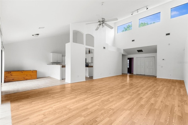 unfurnished living room featuring track lighting, light hardwood / wood-style flooring, a towering ceiling, and ceiling fan