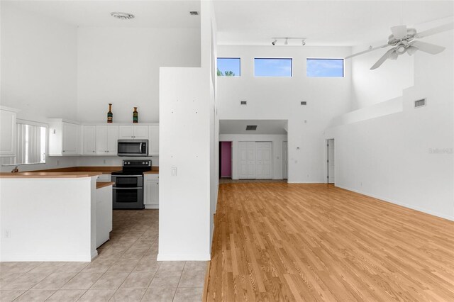 kitchen featuring black electric range, a towering ceiling, white cabinetry, light hardwood / wood-style floors, and ceiling fan