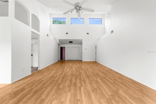 unfurnished living room with a towering ceiling, light hardwood / wood-style flooring, and ceiling fan