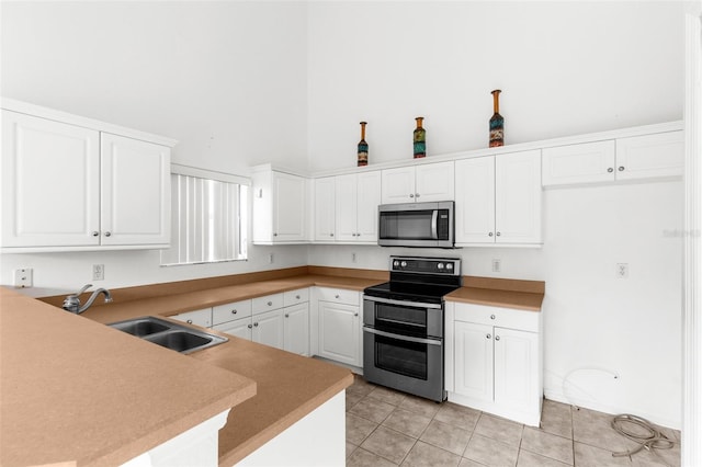 kitchen with appliances with stainless steel finishes, sink, light tile patterned flooring, kitchen peninsula, and white cabinets