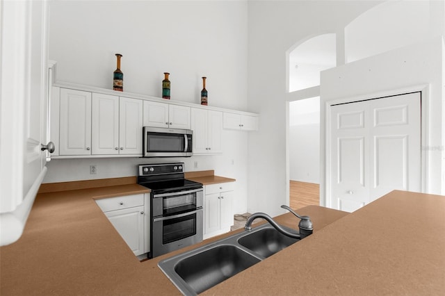 kitchen with appliances with stainless steel finishes, white cabinets, sink, and a towering ceiling