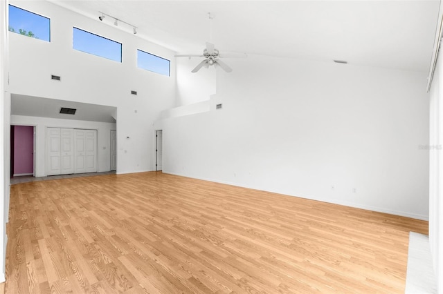 unfurnished living room with light hardwood / wood-style floors, a towering ceiling, track lighting, and ceiling fan