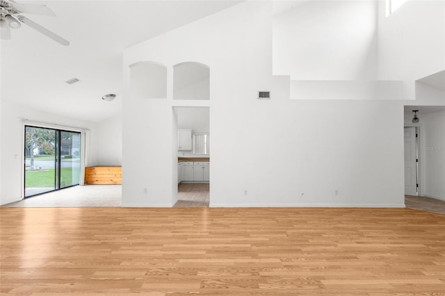 unfurnished living room featuring light wood-type flooring, a towering ceiling, and ceiling fan