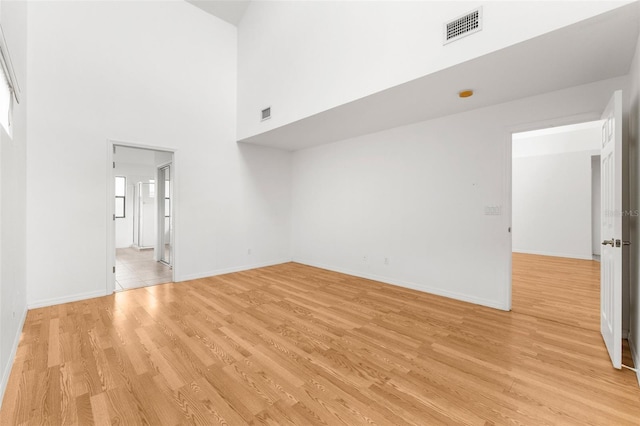 empty room with a towering ceiling and light hardwood / wood-style flooring