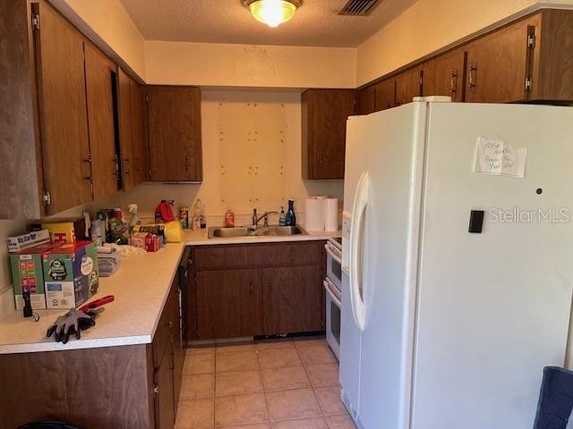 kitchen with white fridge with ice dispenser, a textured ceiling, stainless steel stove, light tile patterned flooring, and sink