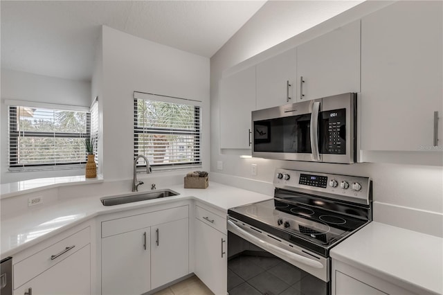 kitchen with lofted ceiling, stainless steel appliances, sink, light tile patterned floors, and white cabinetry