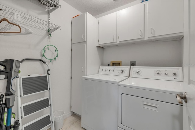 clothes washing area with light tile patterned flooring, independent washer and dryer, a textured ceiling, and cabinets