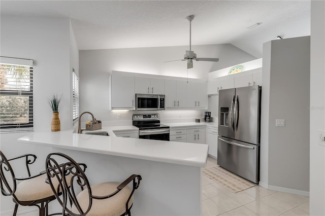 kitchen with appliances with stainless steel finishes, sink, kitchen peninsula, white cabinetry, and vaulted ceiling