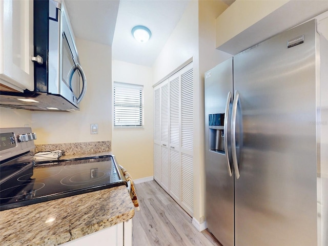 kitchen featuring light wood-type flooring, appliances with stainless steel finishes, light stone countertops, vaulted ceiling, and white cabinets