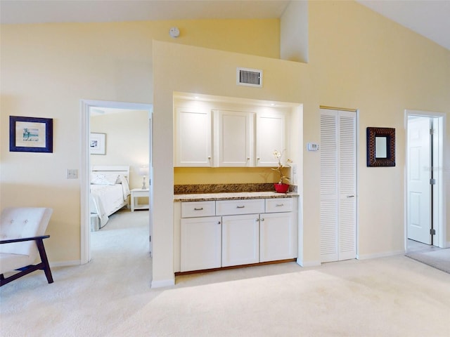 kitchen featuring white cabinets, high vaulted ceiling, and light carpet