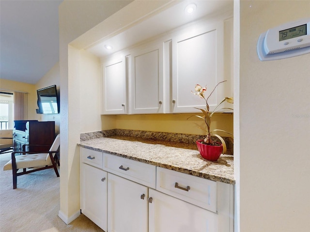 kitchen with white cabinetry, light colored carpet, lofted ceiling, and light stone countertops