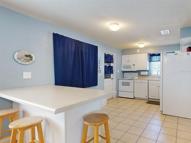 kitchen featuring white cabinetry, kitchen peninsula, a breakfast bar area, a textured ceiling, and white appliances