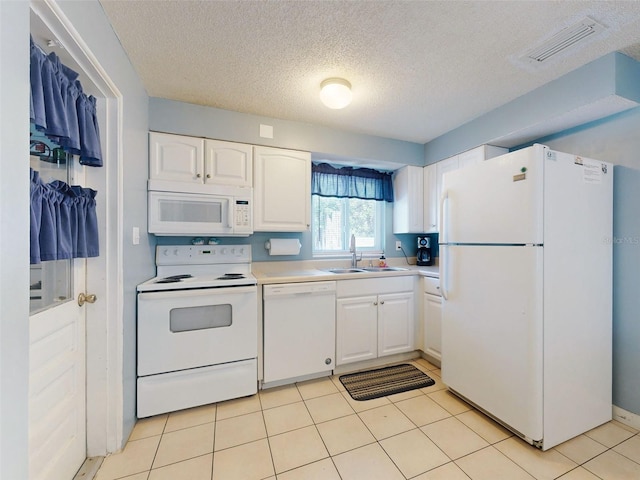 kitchen featuring a textured ceiling, sink, light tile patterned flooring, white cabinetry, and white appliances