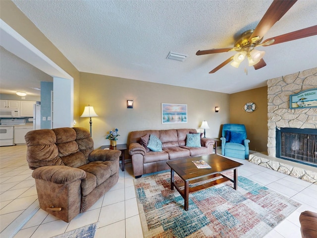 tiled living room with a fireplace, ceiling fan, and a textured ceiling