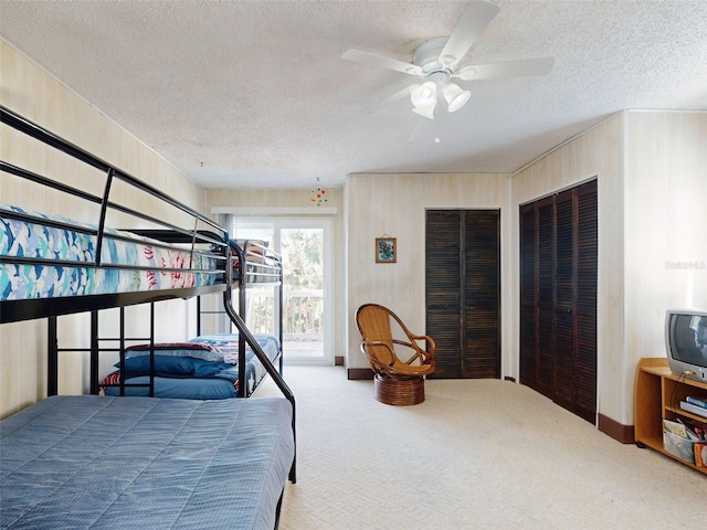 carpeted bedroom with a textured ceiling, ceiling fan, and two closets