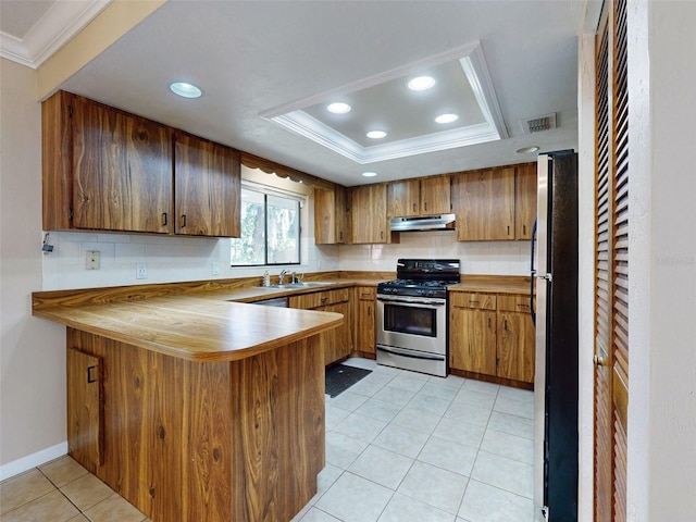 kitchen with kitchen peninsula, decorative backsplash, ornamental molding, stainless steel appliances, and a raised ceiling