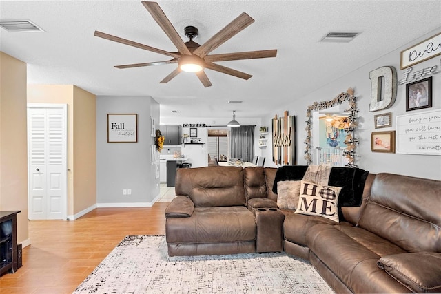 living room featuring light hardwood / wood-style floors, ceiling fan, and a textured ceiling